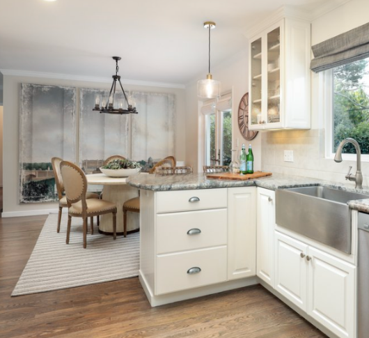White kitchen looking into a dining room with lights. Stainless steel sink. Art on the wall from ceiling to the floor. Striped rug (brown and white). Modren looking kitchen. Make A Small Room Look Bigger